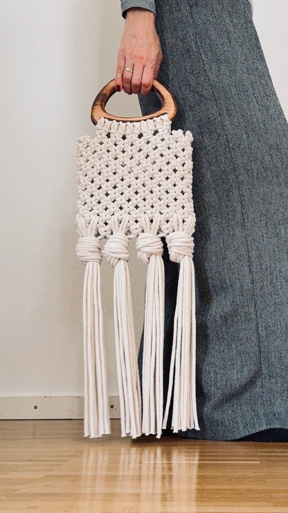 Macrame handbag with tassels held by a person wearing gray pants.