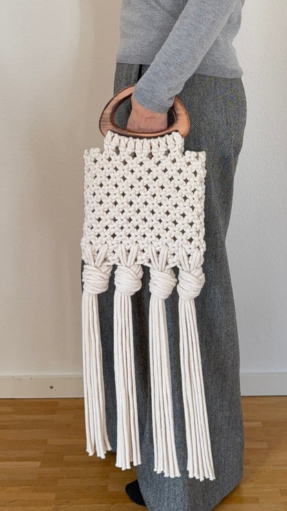 Macrame handbag with tassels held by a person wearing gray pants and a gray sweater.