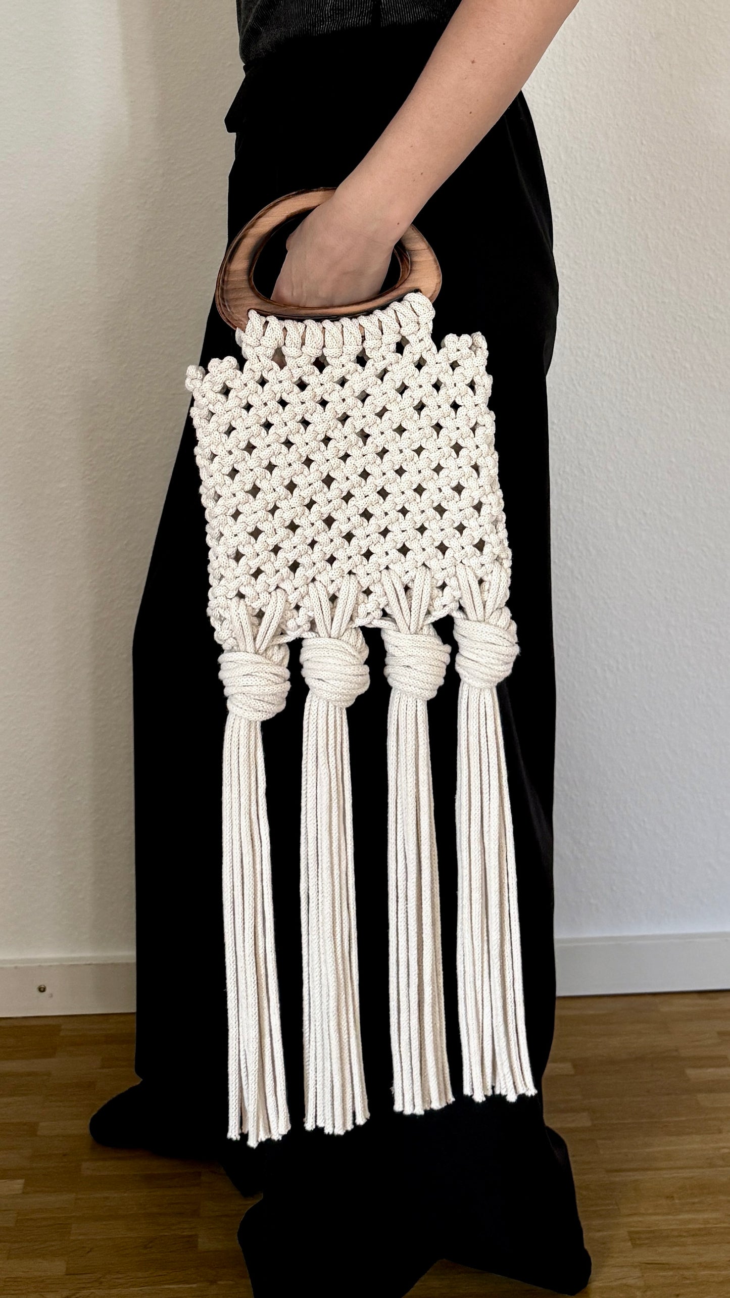 White macrame clutch held by a person wearing a black dress against a plain background