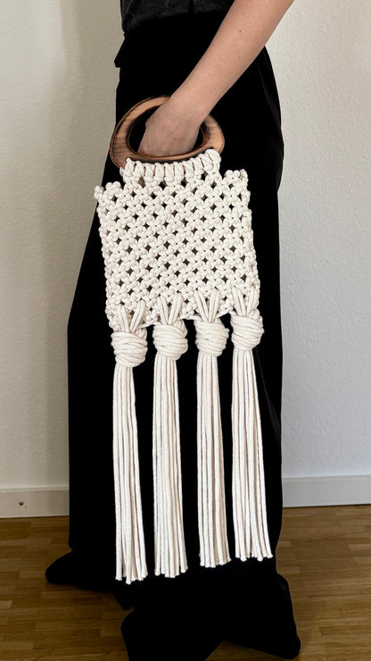 White macrame clutch held by a person wearing a black dress against a plain background