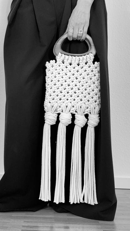 White macrame handbag with tassels held by a person wearing a black outfit.