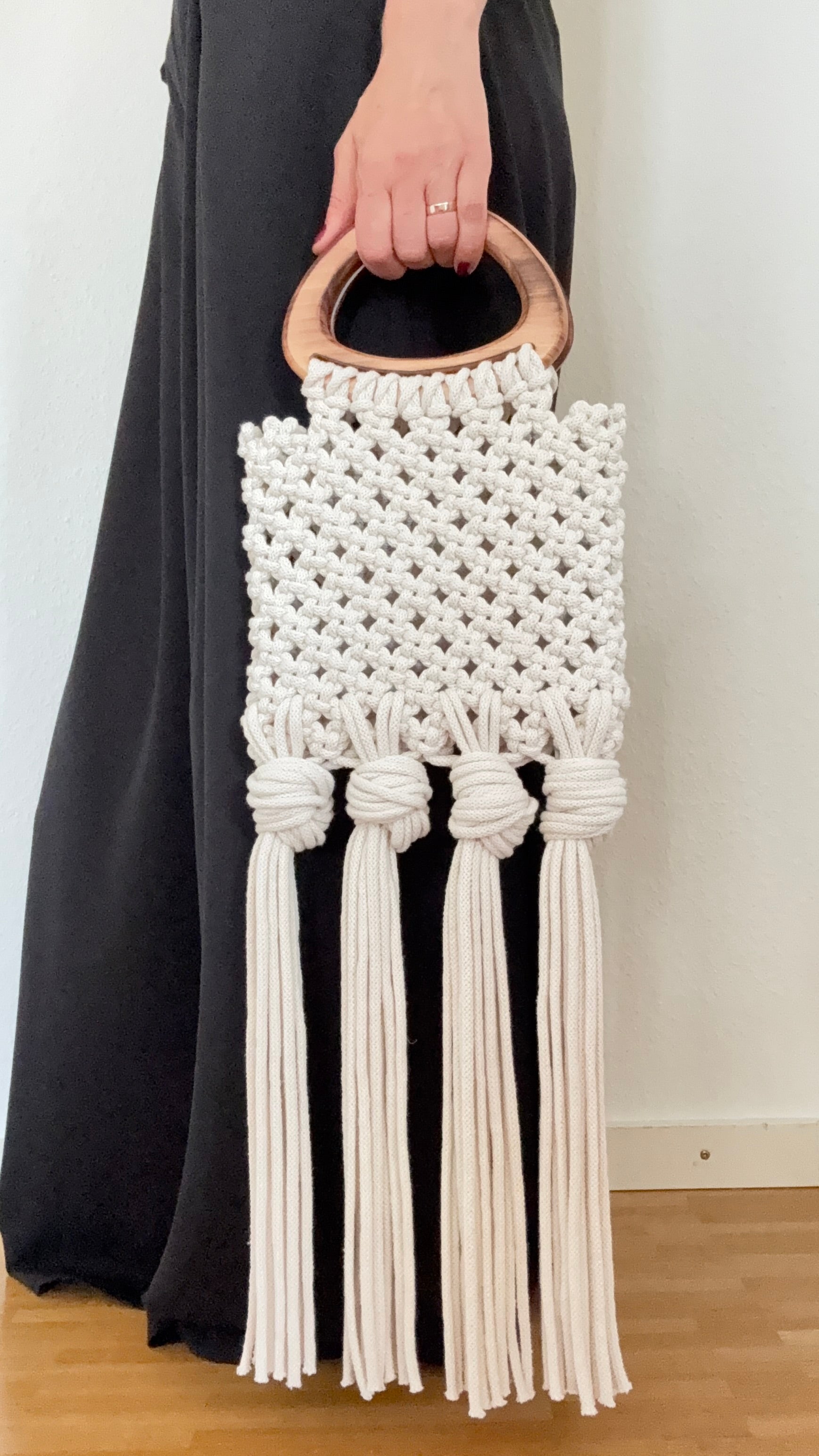 White macrame handbag with wooden handle held by a person wearing a black dress.