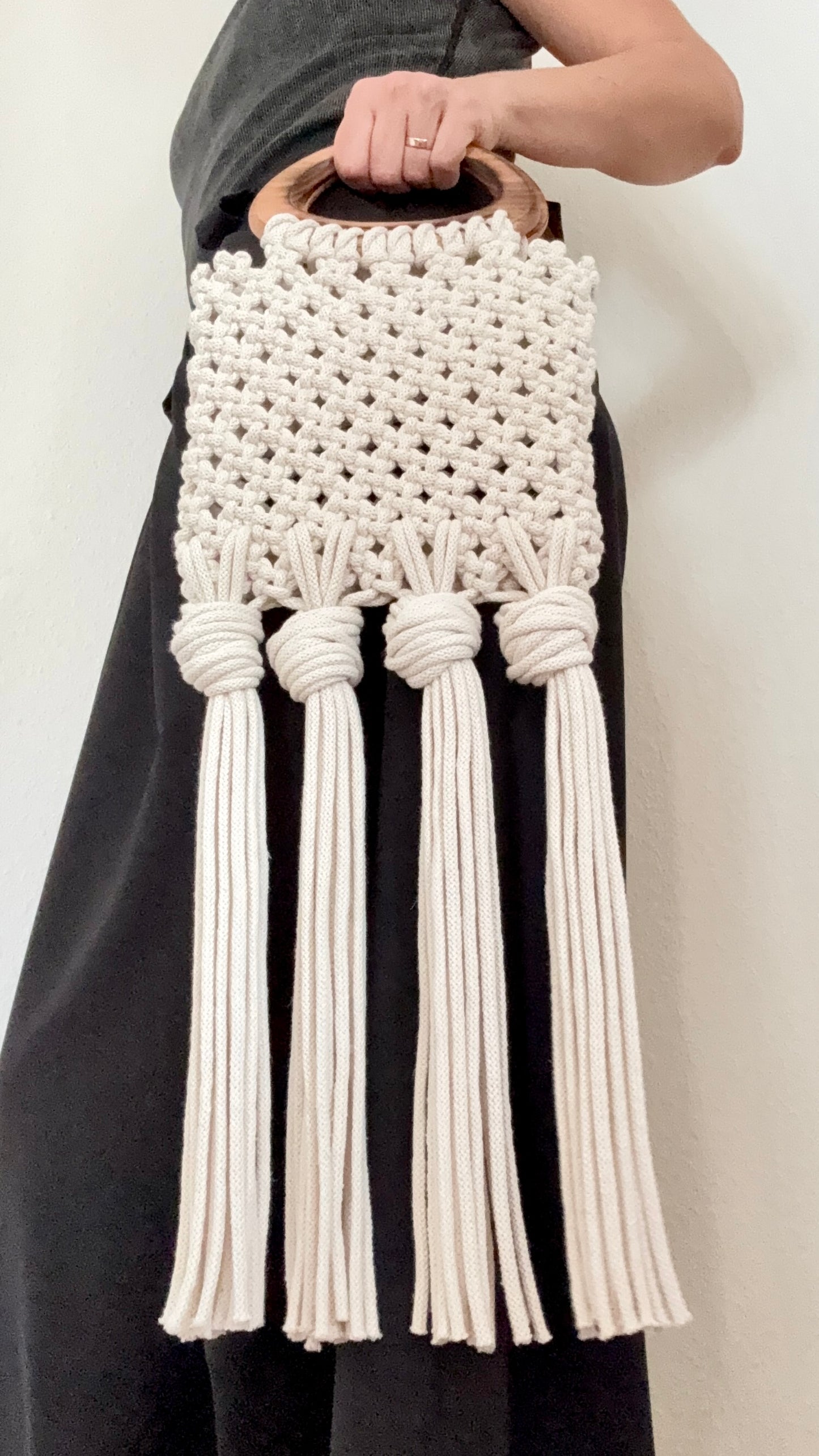 White macrame handbag with tassels held by a person against a neutral background