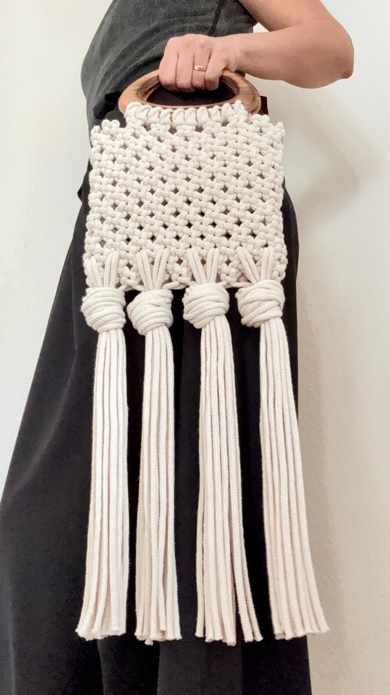 White macrame handbag with tassels held by a person against a neutral background
