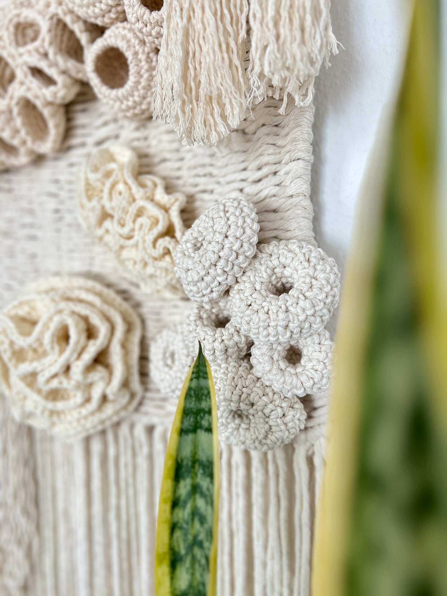 Close-up of a textured wall art piece with coral reef details and tassels.
