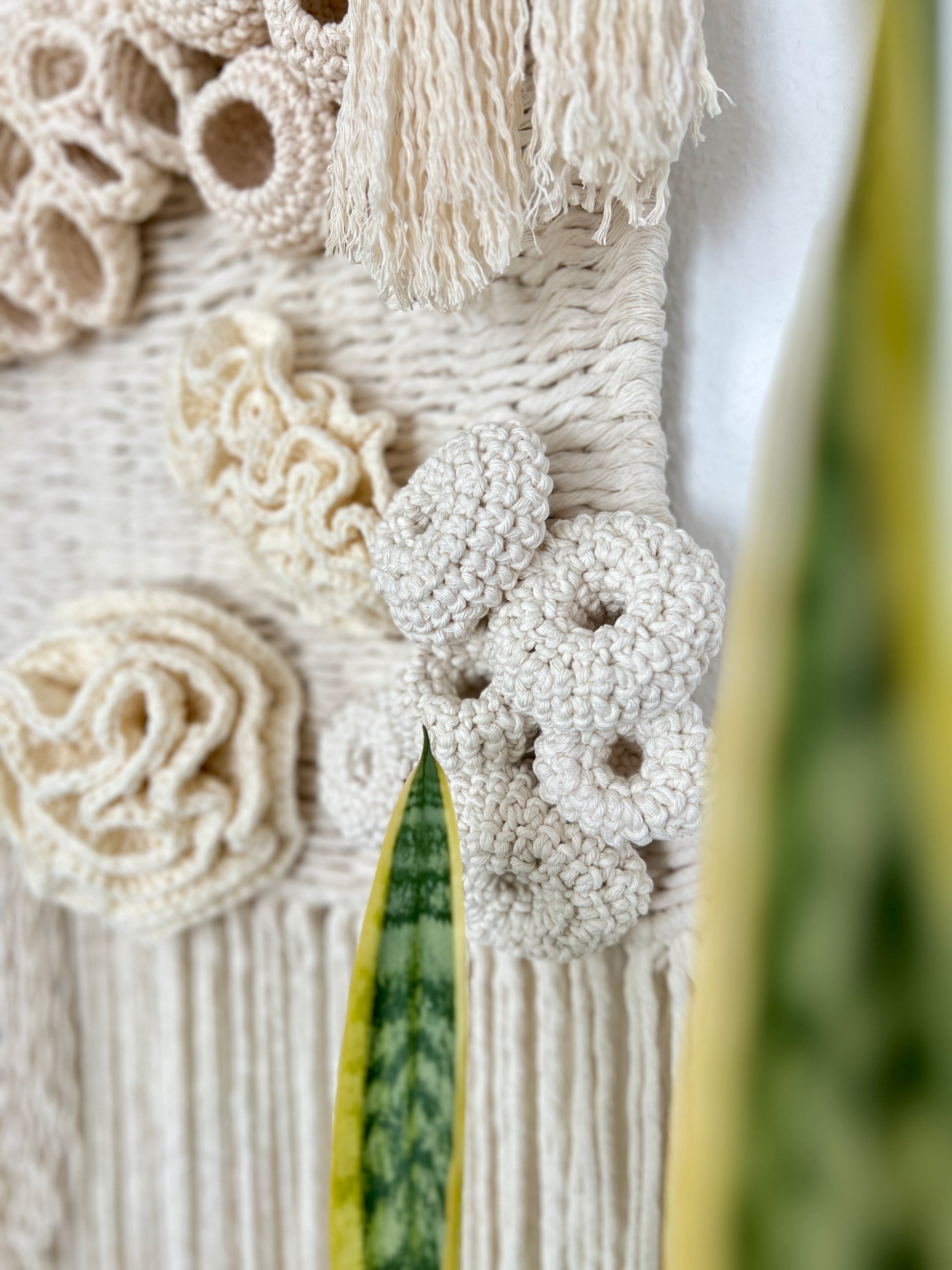 Close-up of a textured wall art piece with coral reef details and tassels.