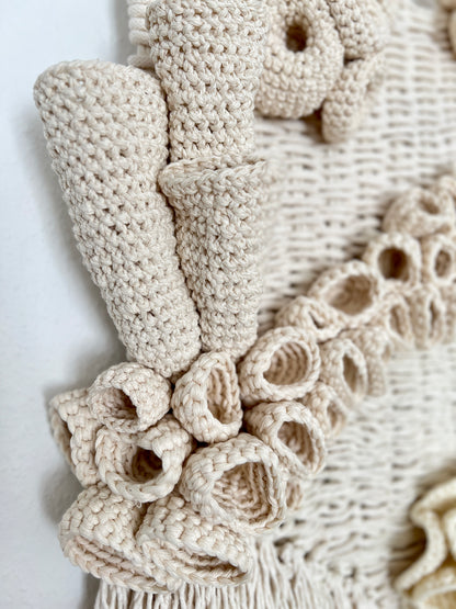 Close-up of a beige crochet wall hanging with decorative details on a white background