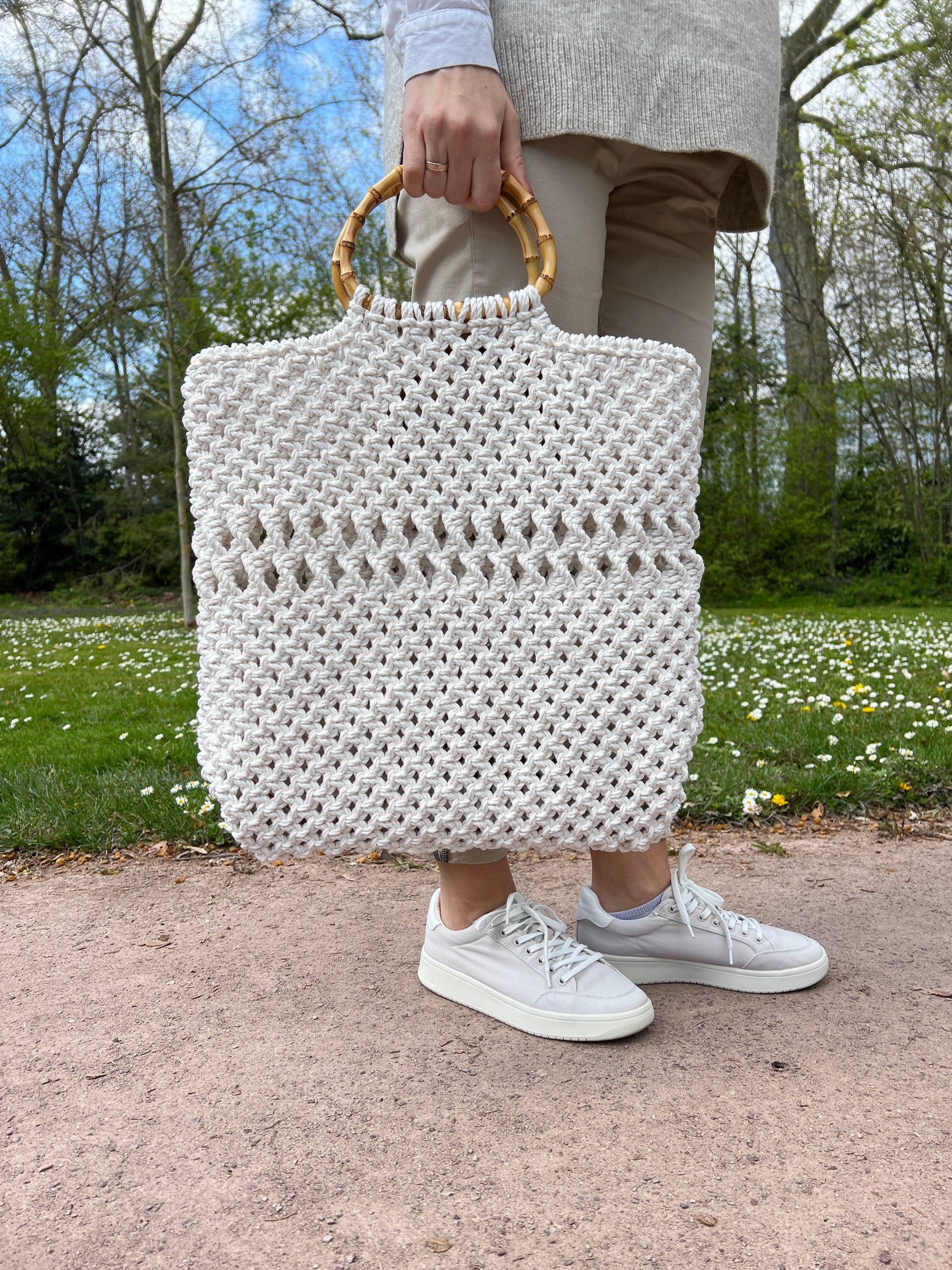 Person holding a white textured macrame tote bag outdoors on a sunny day