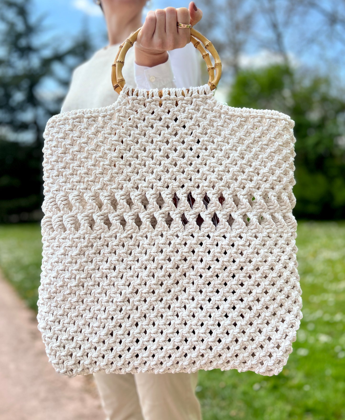 White woven handbag with bamboo handle held by a person outdoors.