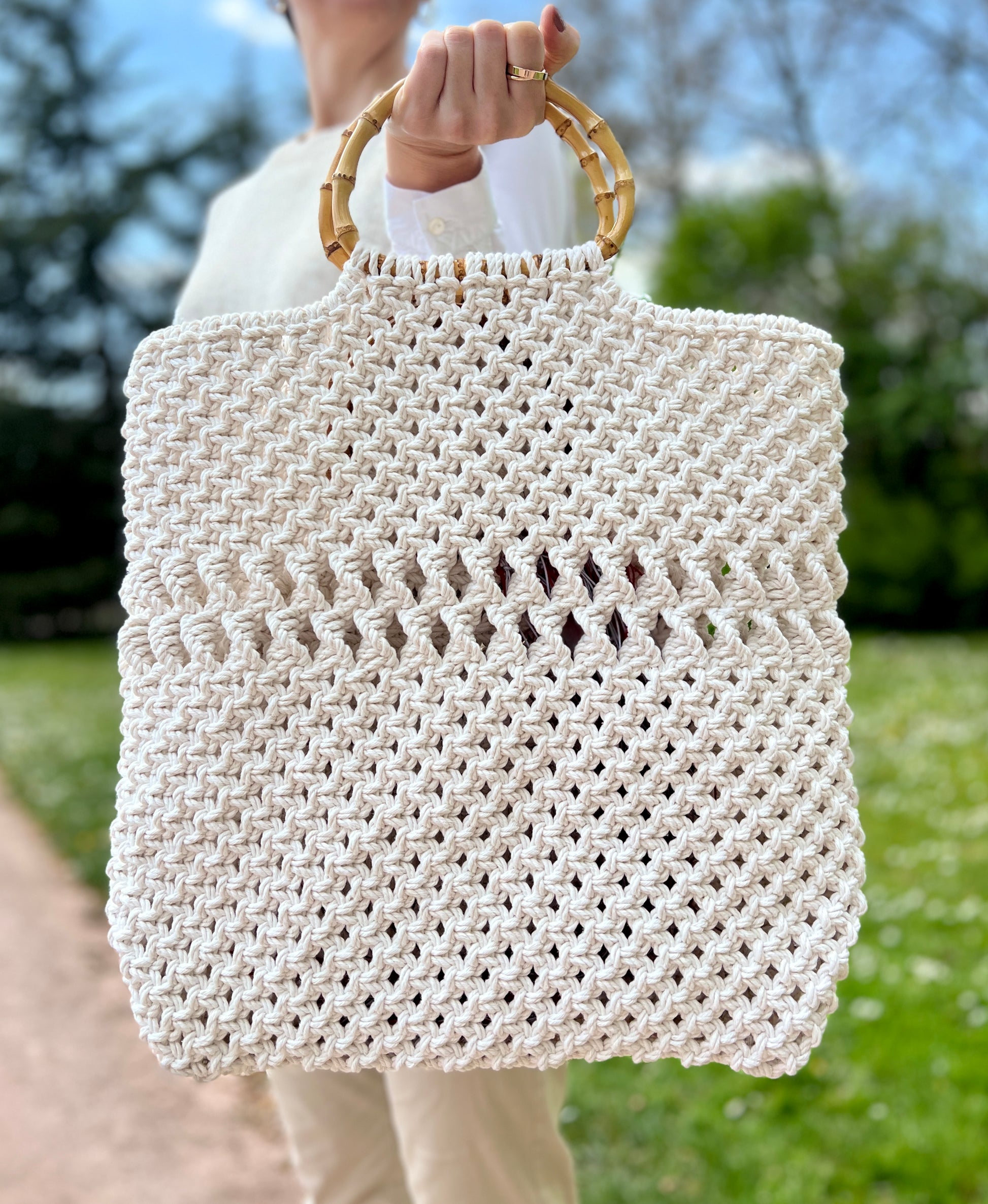 White woven handbag with bamboo handle held by a person outdoors.