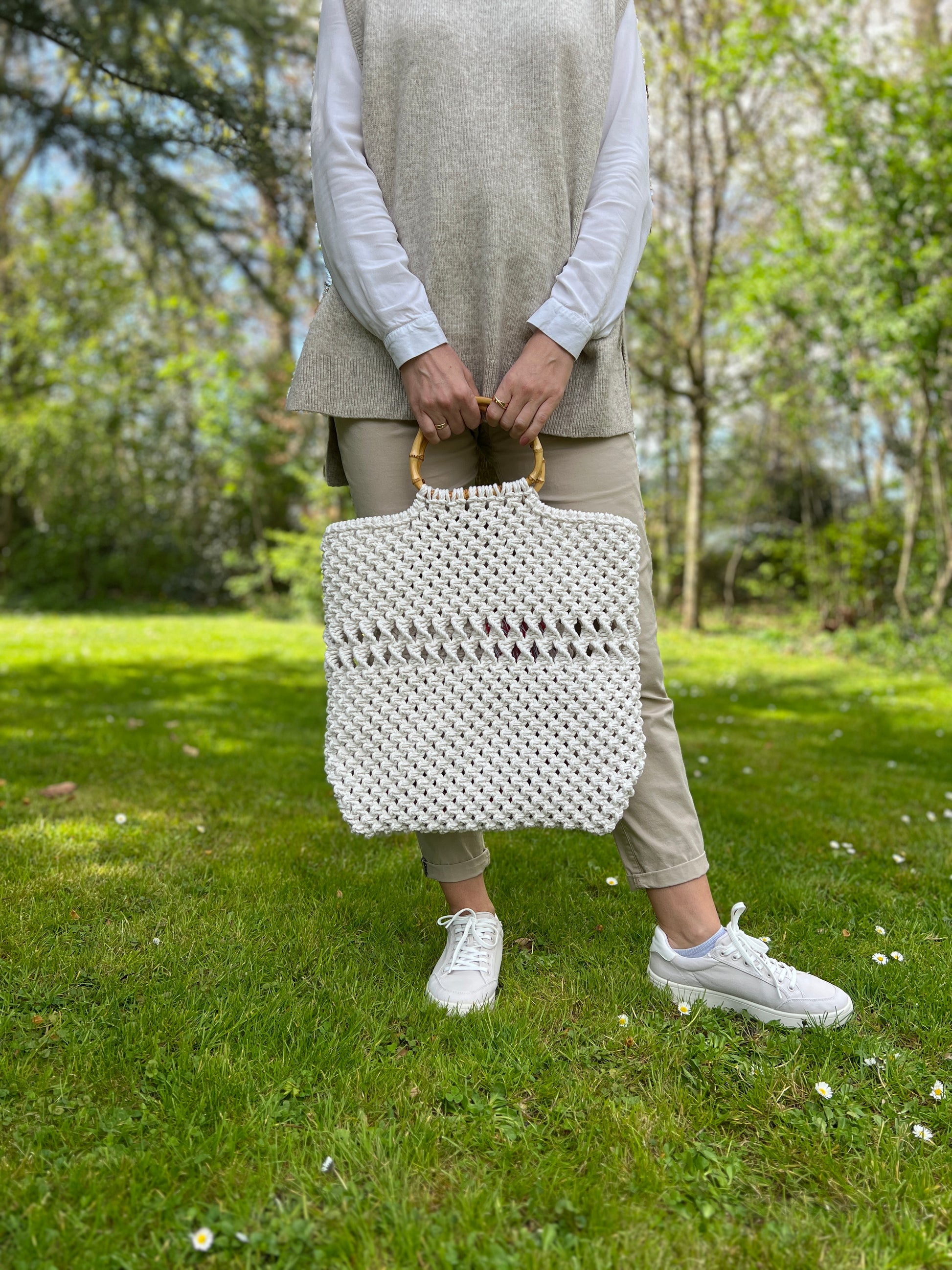 Person holding a white woven macrame bag outdoors in a park