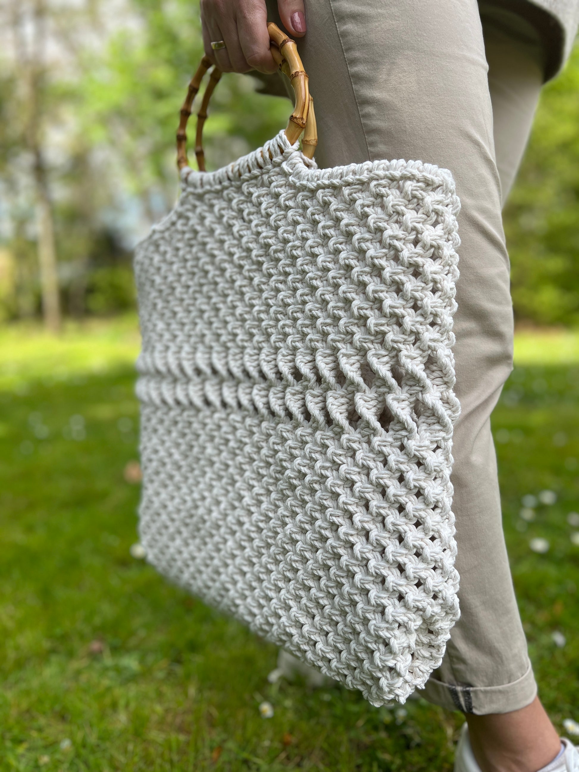 Person holding a textured macrame tote handbag with a blurred green outdoor background