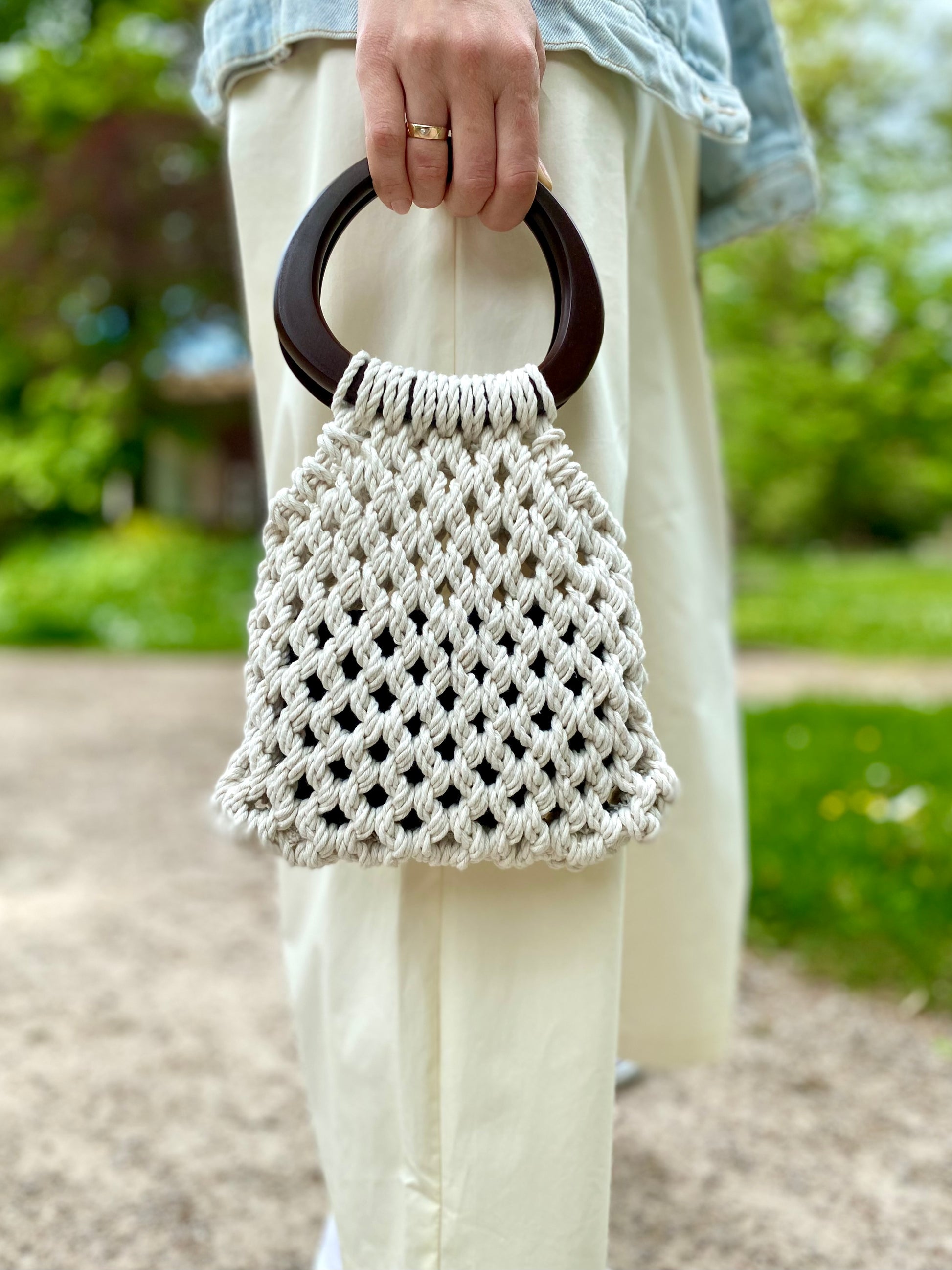 Person holding a macrame handbag with wooden handle outdoors.