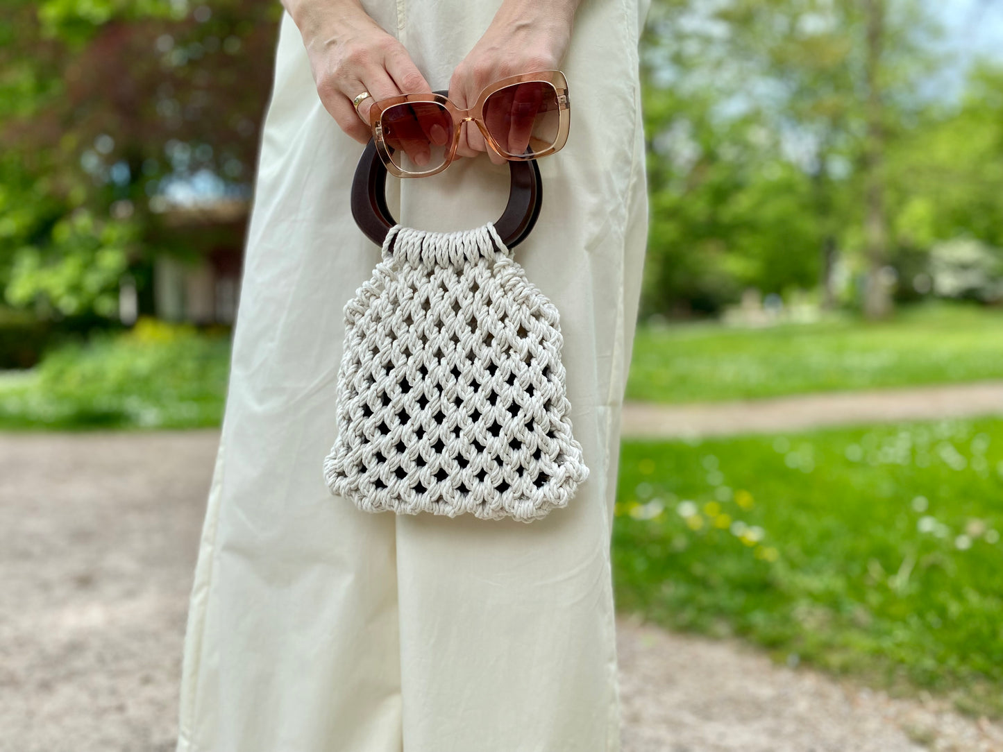 Person holding a macrame handbag with sunglasses on a blurred outdoor background