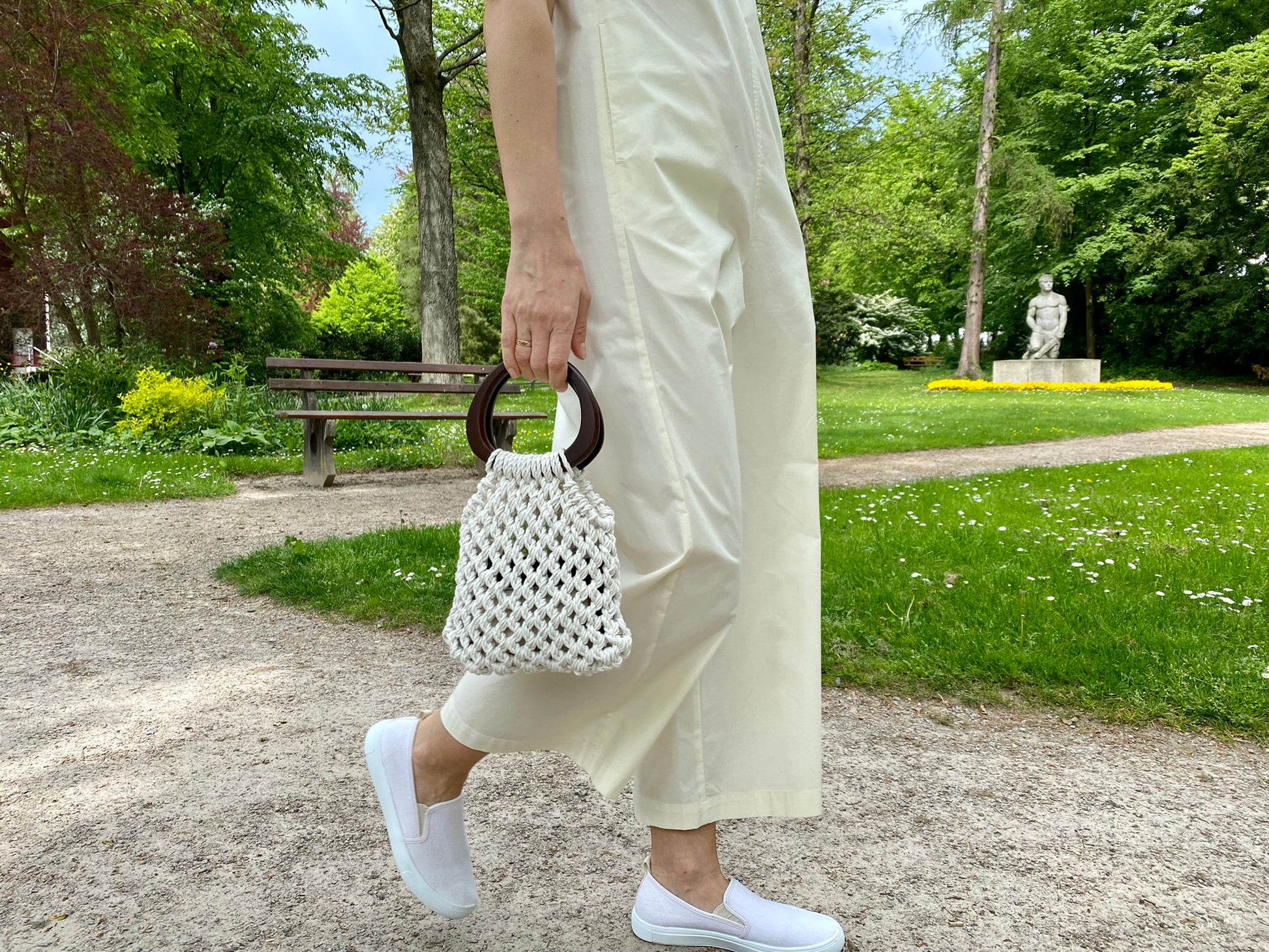 Person holding a white textured macrame handbag in a park setting