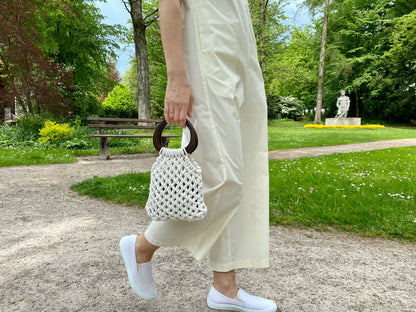 Person holding a white textured macrame handbag in a park setting