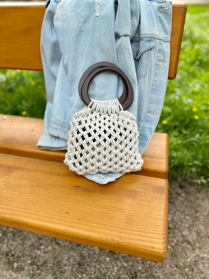 Macrame handbag with wooden handle on a denim jacket over a wooden bench outdoors.