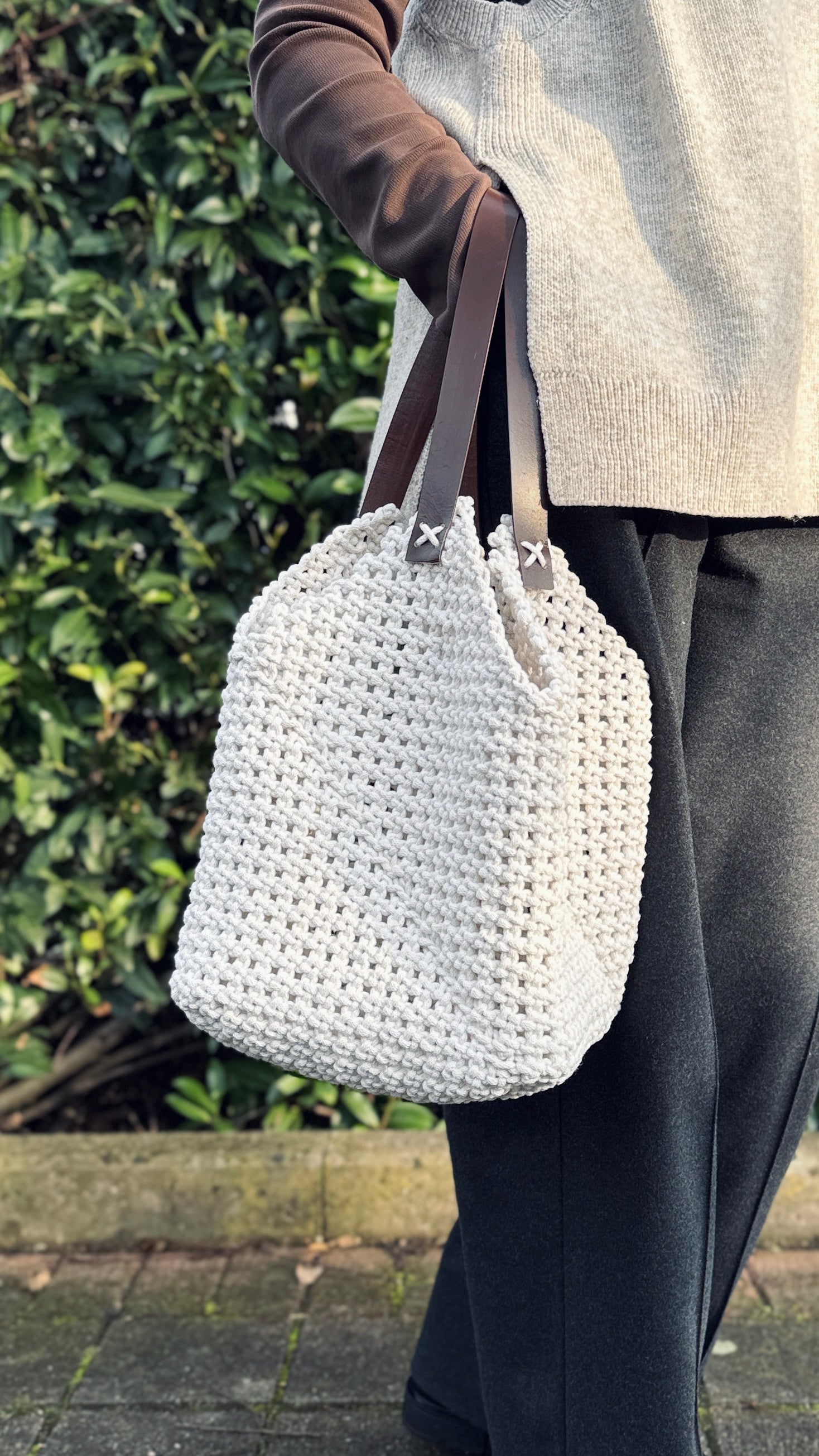 Person holding a white woven handbag with a blurred green background
