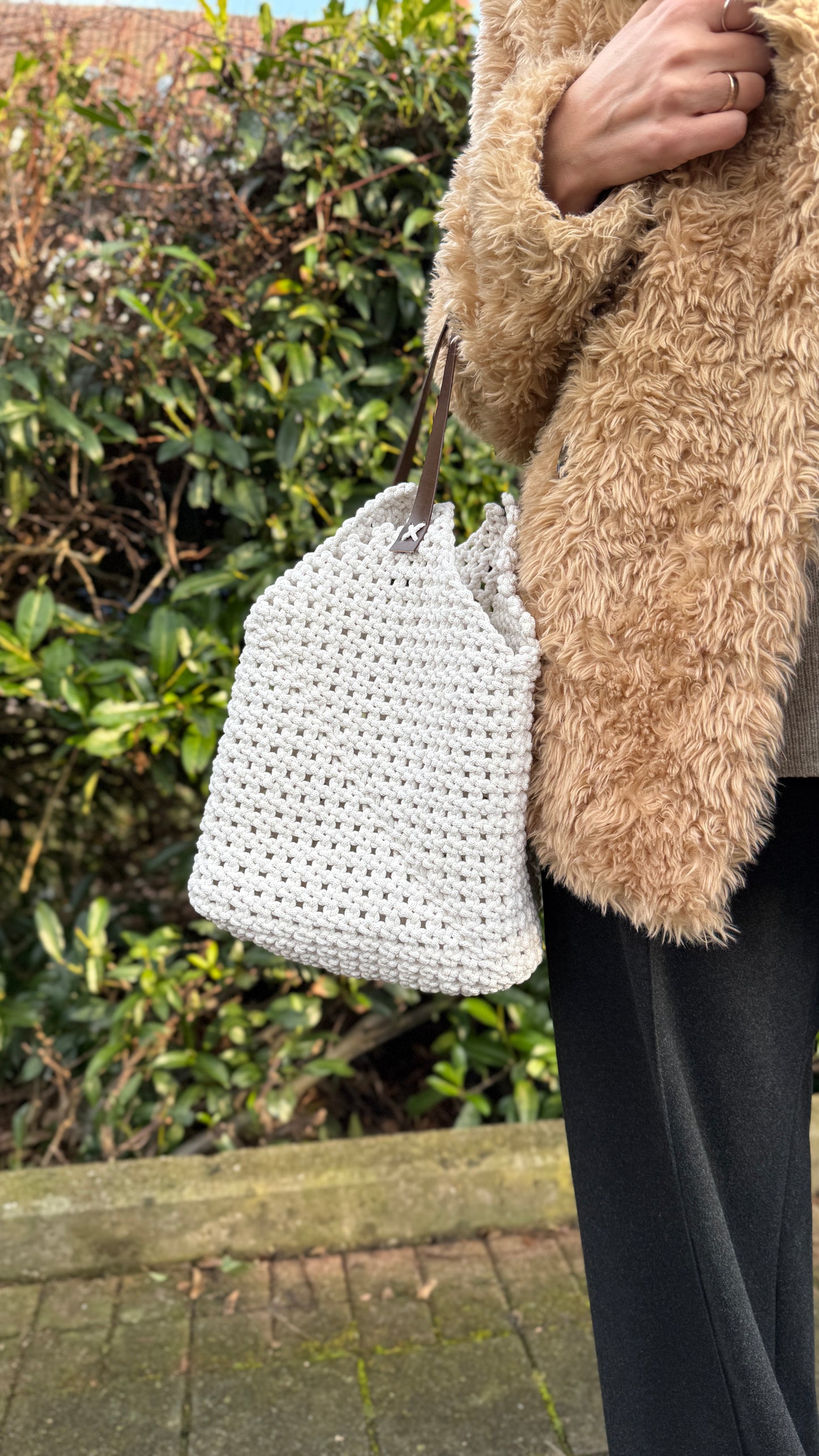 Person holding a white woven bag with a blurred natural background