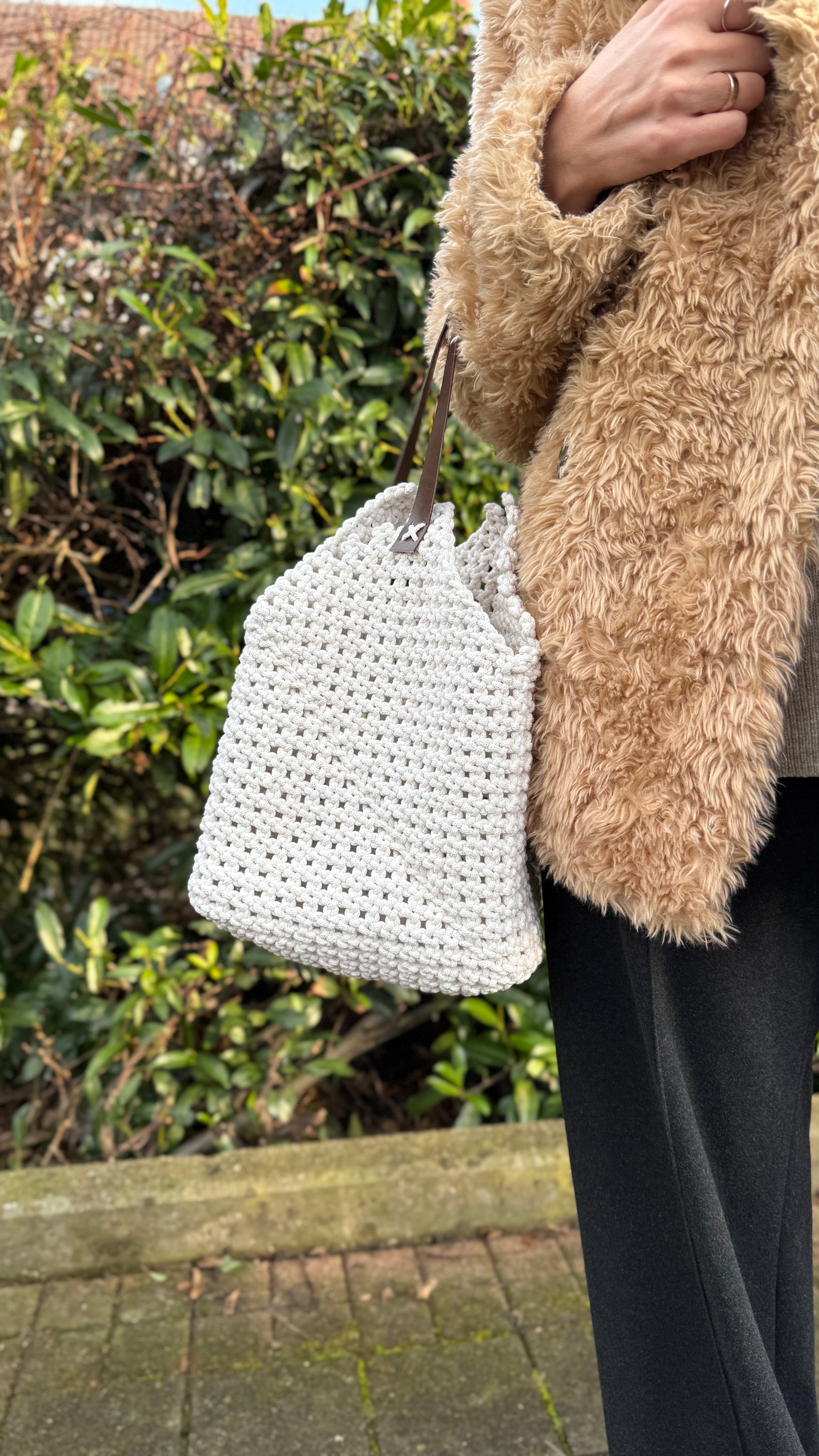Person holding a white woven bag with a blurred natural background