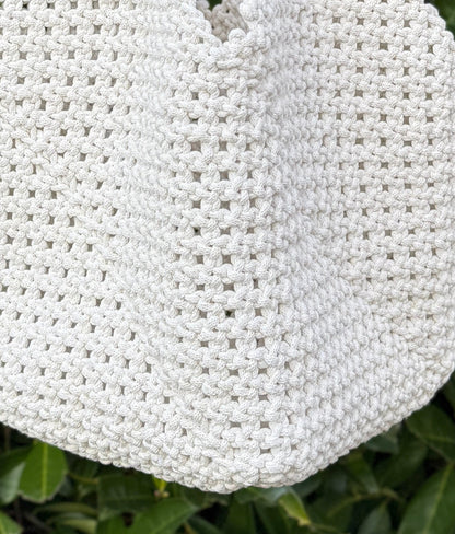 White woven handbag with brown handles held by a person against a green leafy background