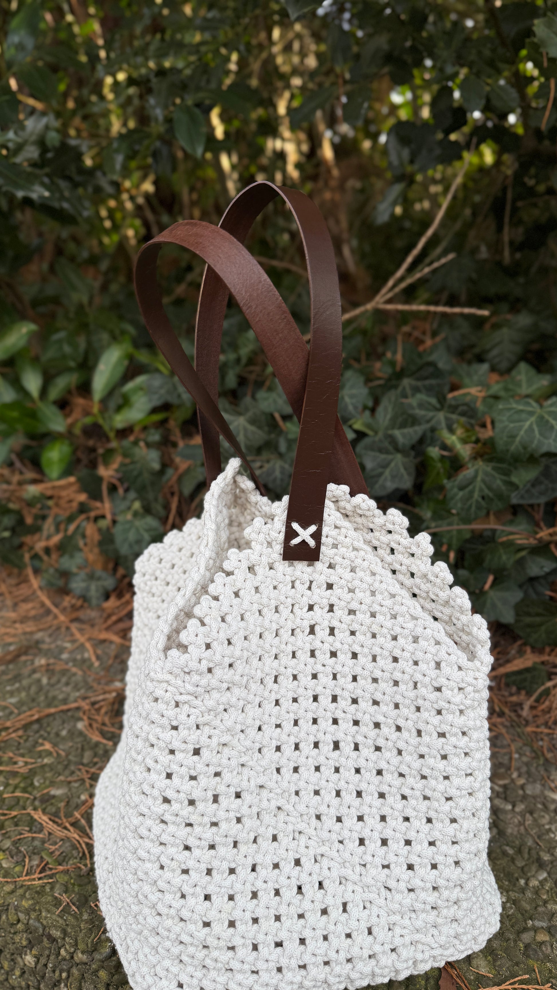 White woven bag with brown leather straps on a natural background