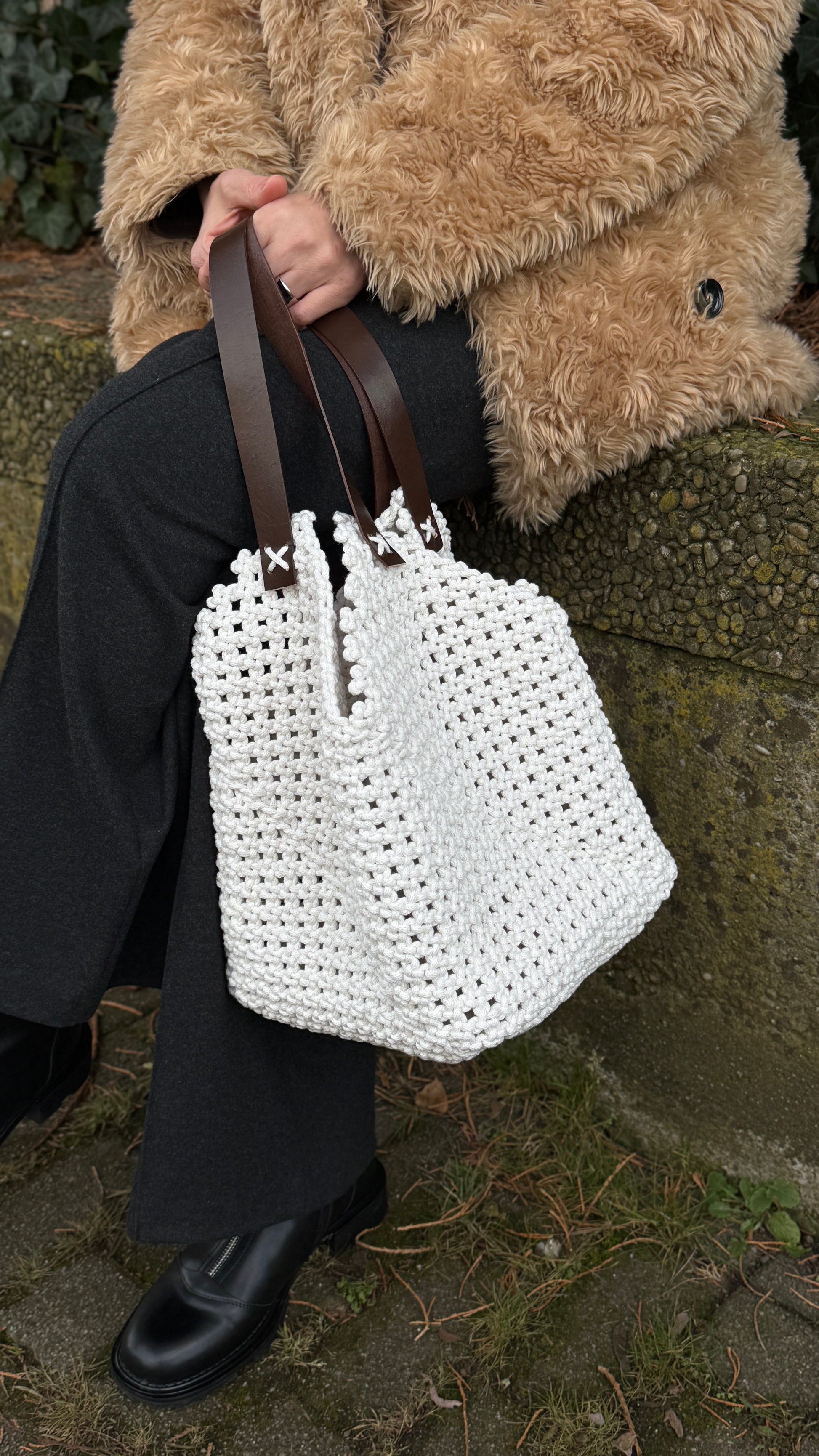 Person holding a white woven handbag with a textured surface, wearing a fur coat.
