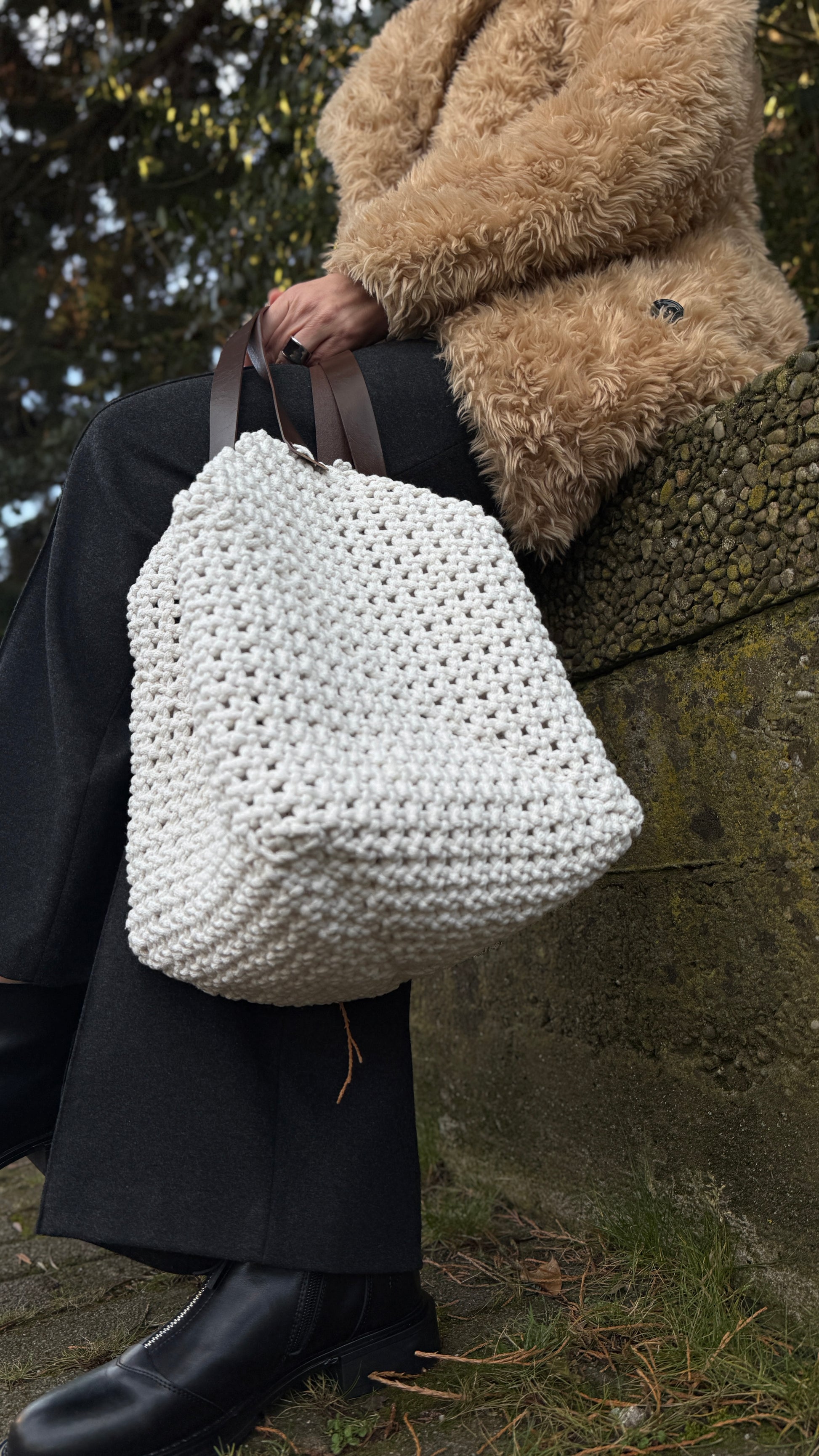 Person holding a large white macrame bag outdoors.