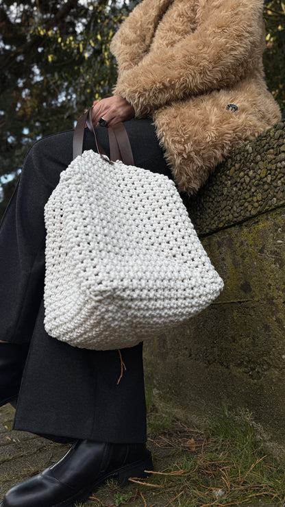 Person holding a large white macrame bag outdoors.