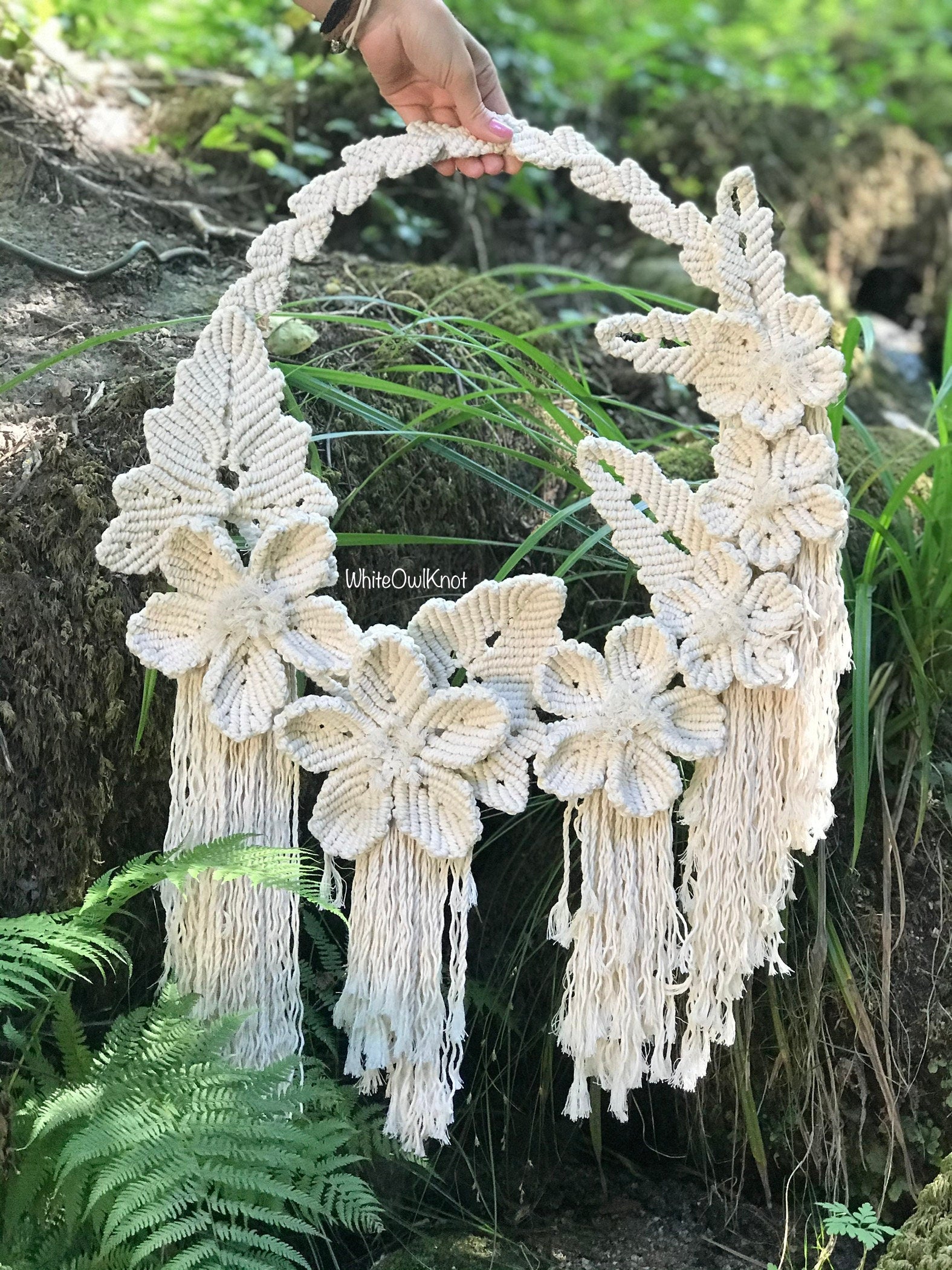 Macrame wall hanging with floral designs held by a hand against a natural background.