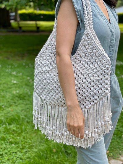 Woman holding a woven bag with fringes outdoors on a grassy area
