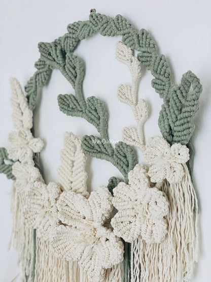 Macrame wall hanging with green and white leaves and flowers on a light background
