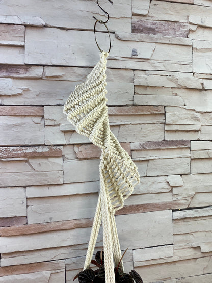 Macrame plant hanger hanging against a stone wall.