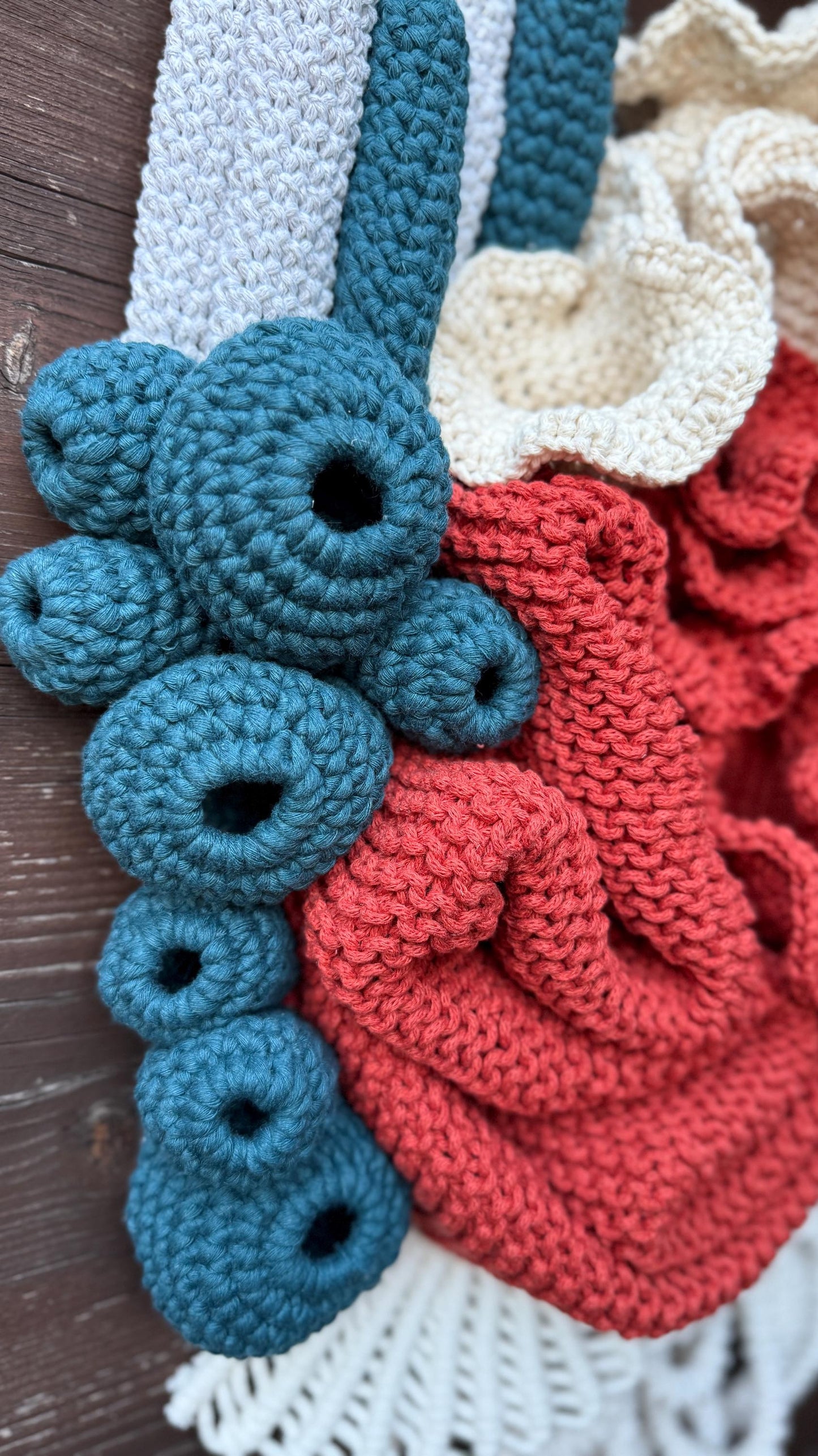 Close-up of crocheted coral reef items including blue, red, and white pieces on a wooden surface.