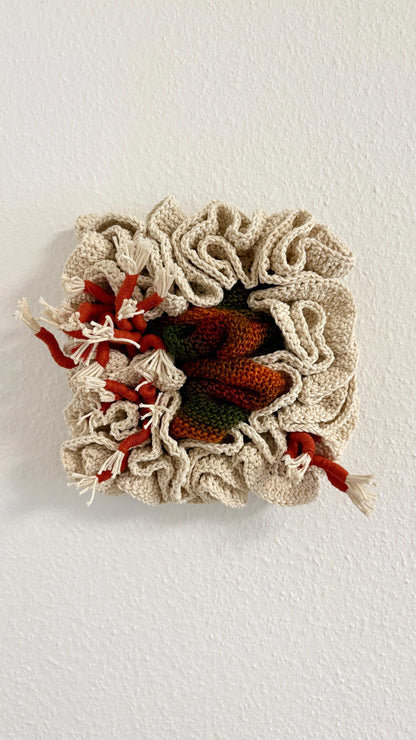 Crocheted wall art piece with red and green accents on a white background
