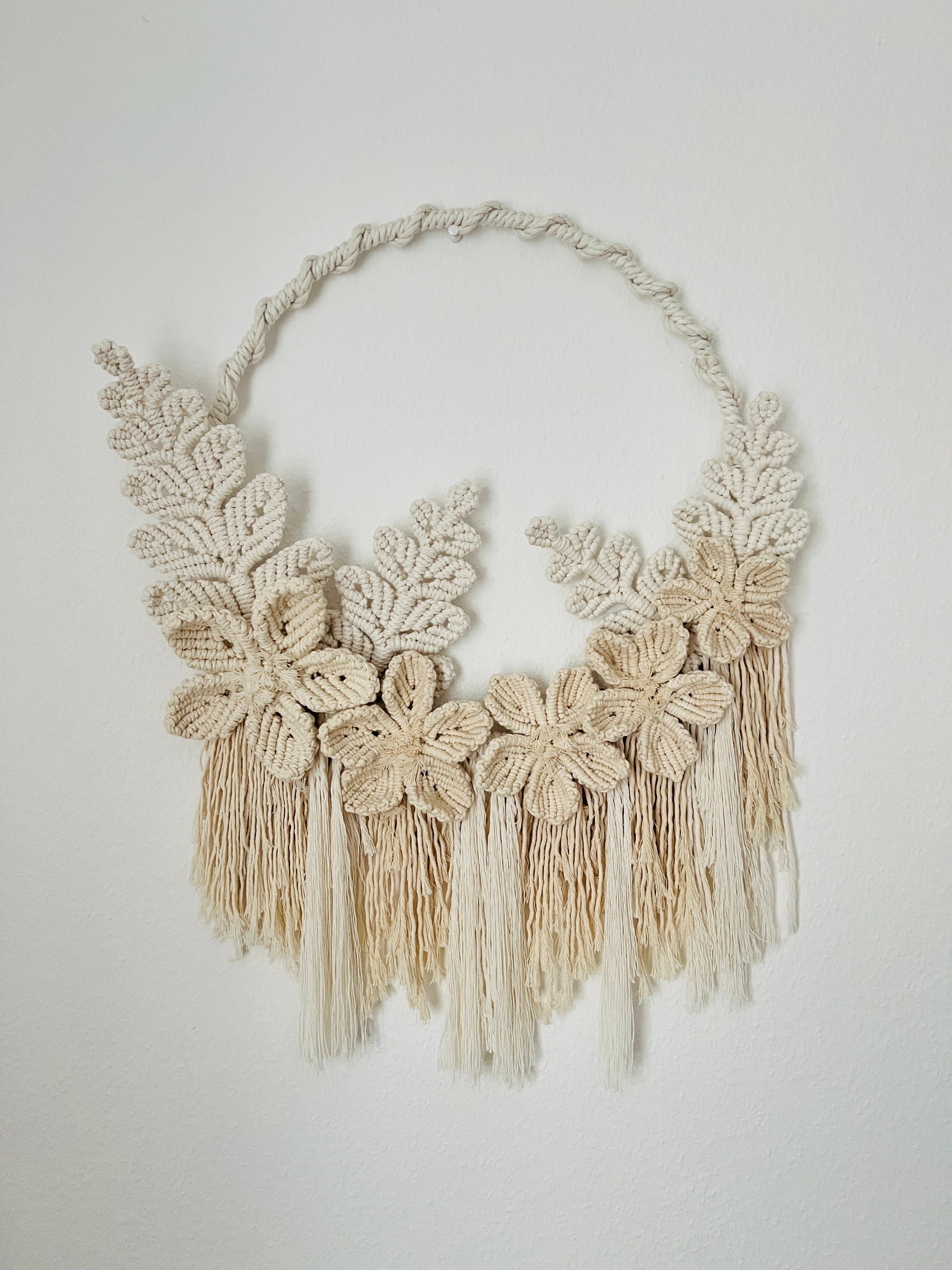 Beige macrame necklace with floral designs and tassels on a light gray background