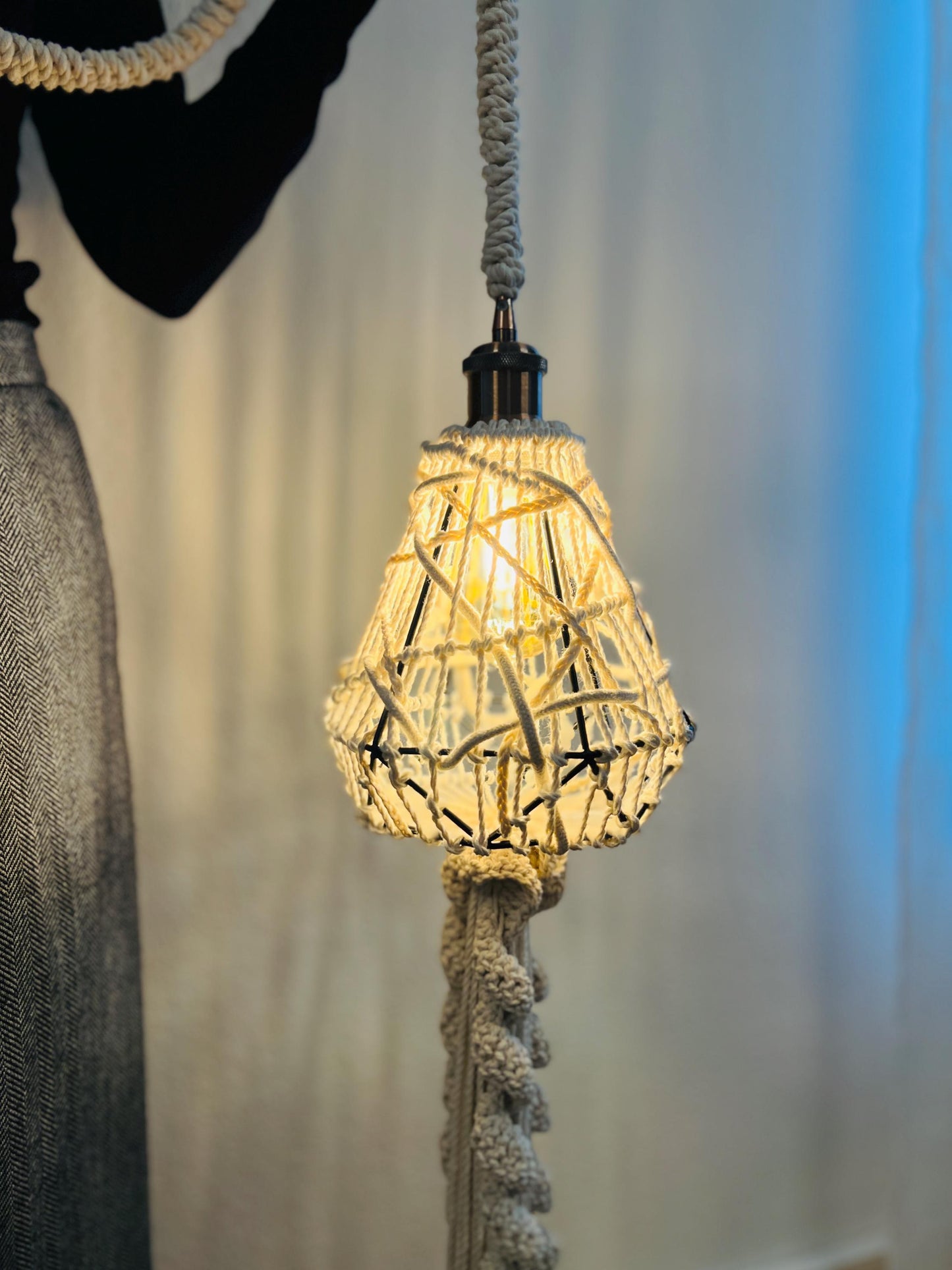 Decorative lightshade with woven design hanging by a rope against a neutral background