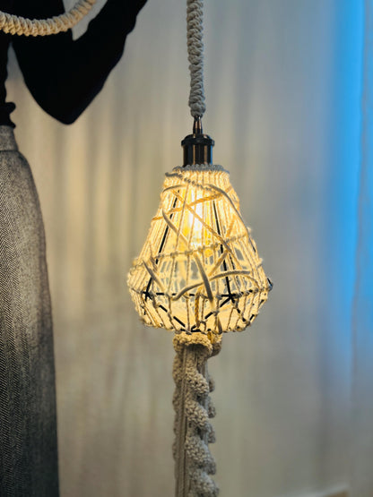 Decorative lightshade with woven design hanging by a rope against a neutral background