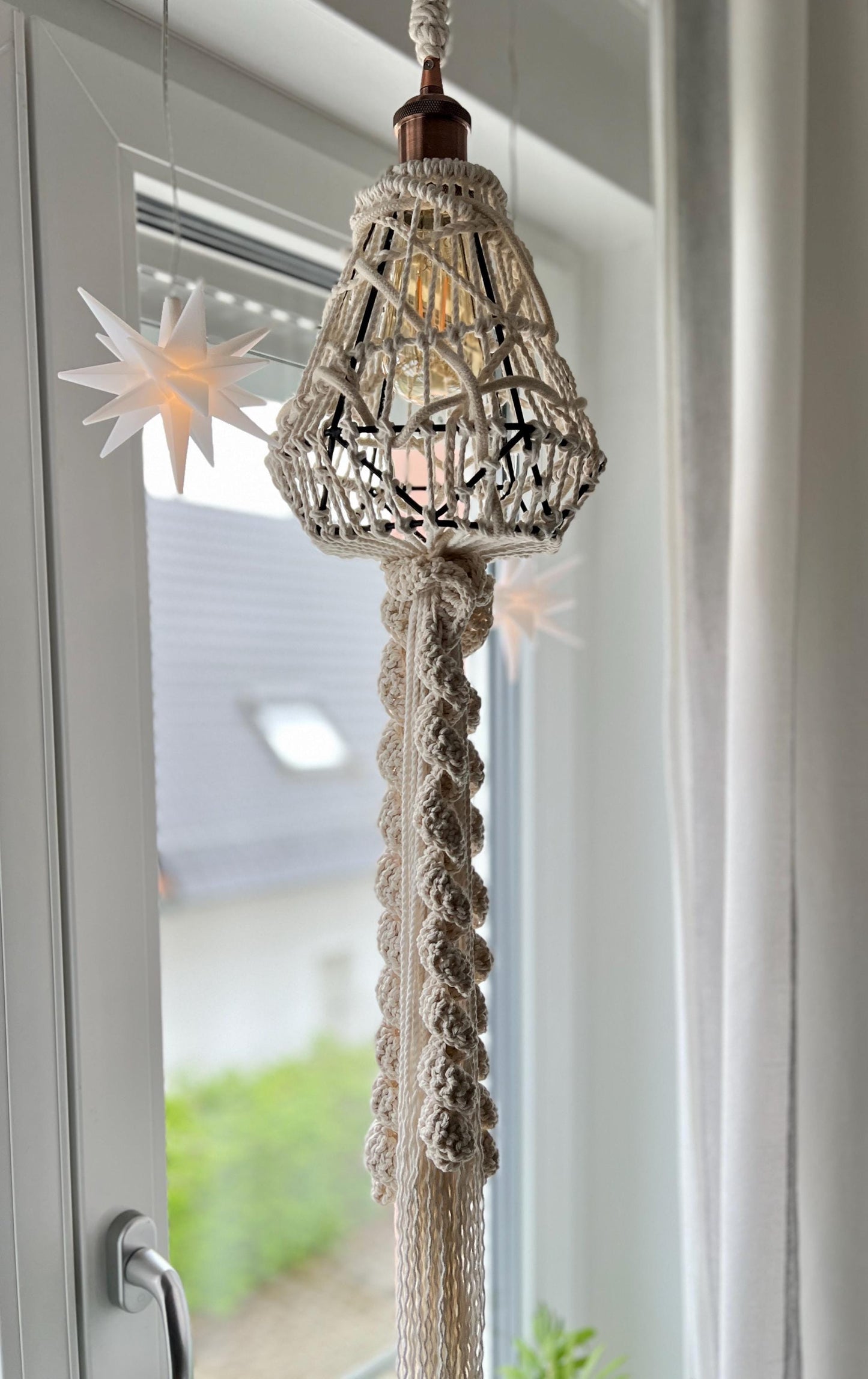Decorative hanging lamp fixture with macrame cord against a window background