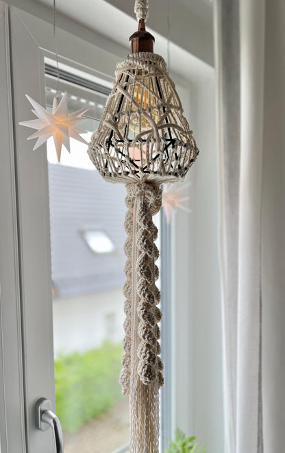 Decorative hanging lamp fixture with macrame cord against a window background