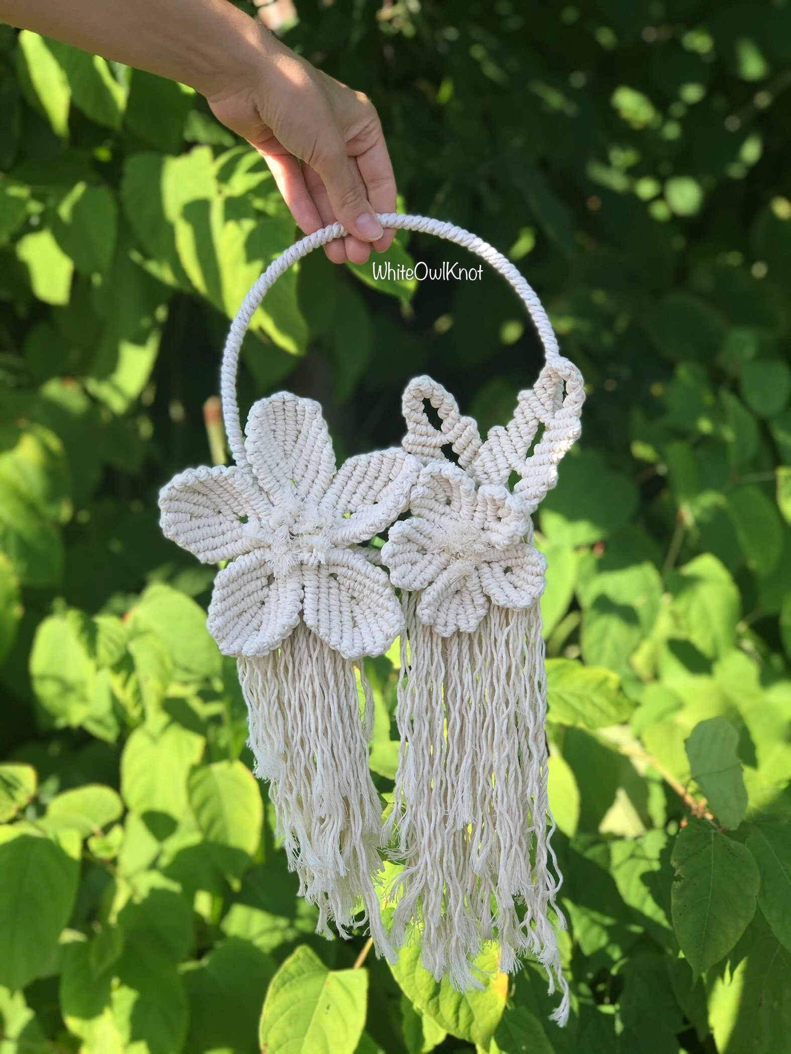 Handmade macrame bag with floral designs held against a green leafy background
