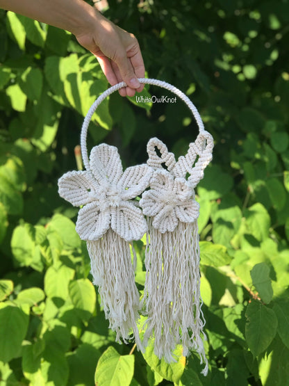 Handmade macrame bag with floral designs held against a green leafy background