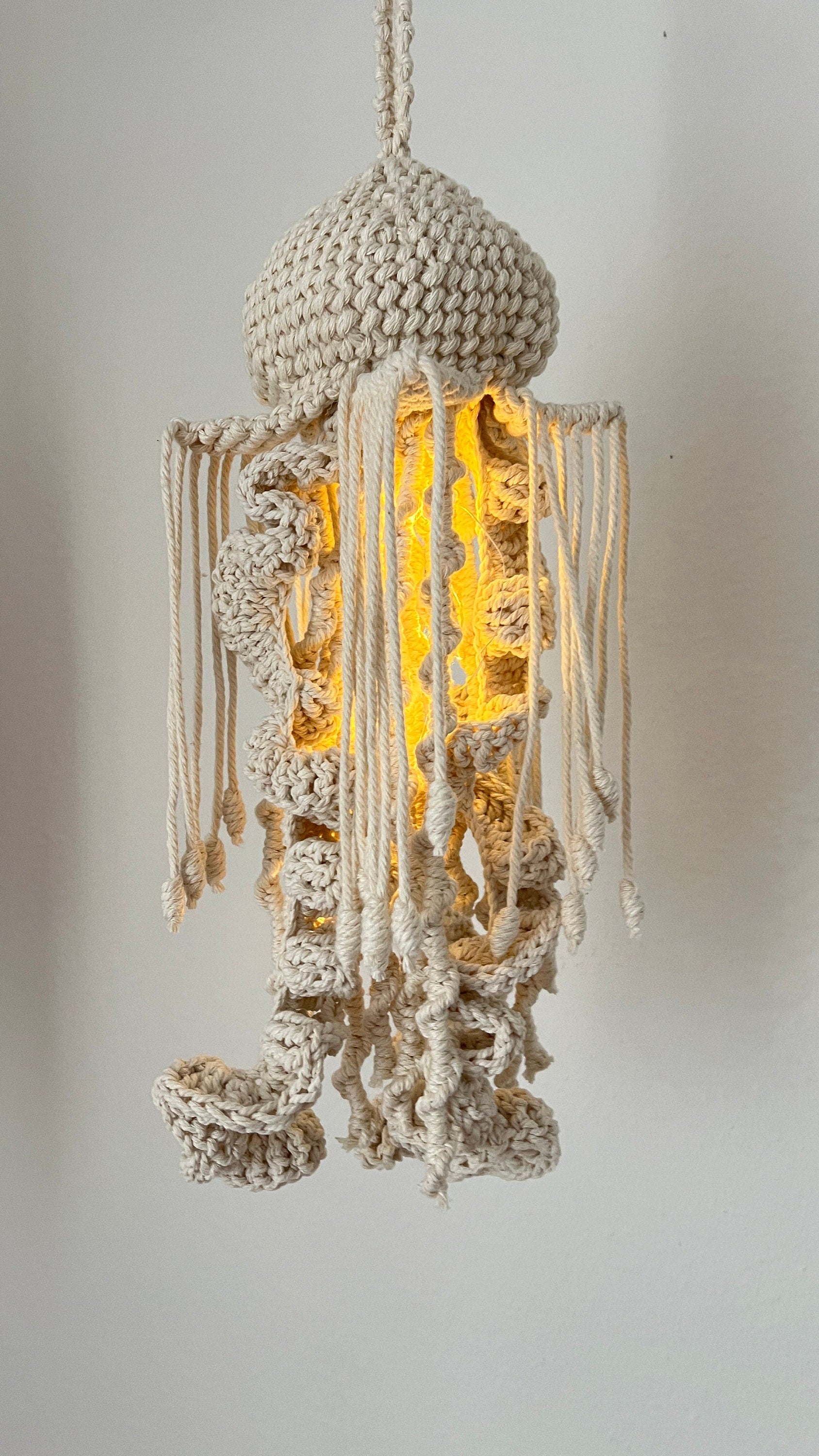 Macrame jellyfish pendant light with a warm glow on a plain background