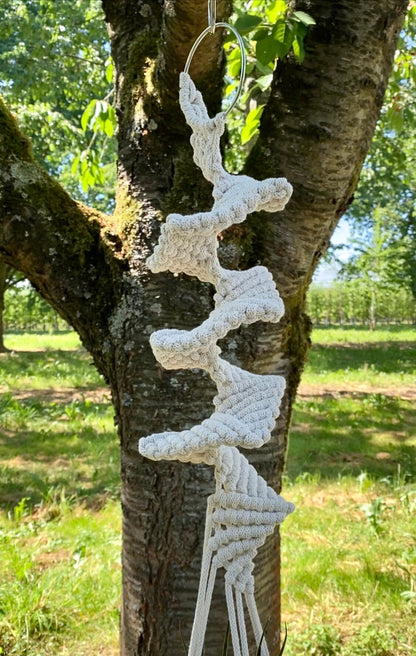 White macrame wall hanging on a tree branch outdoors