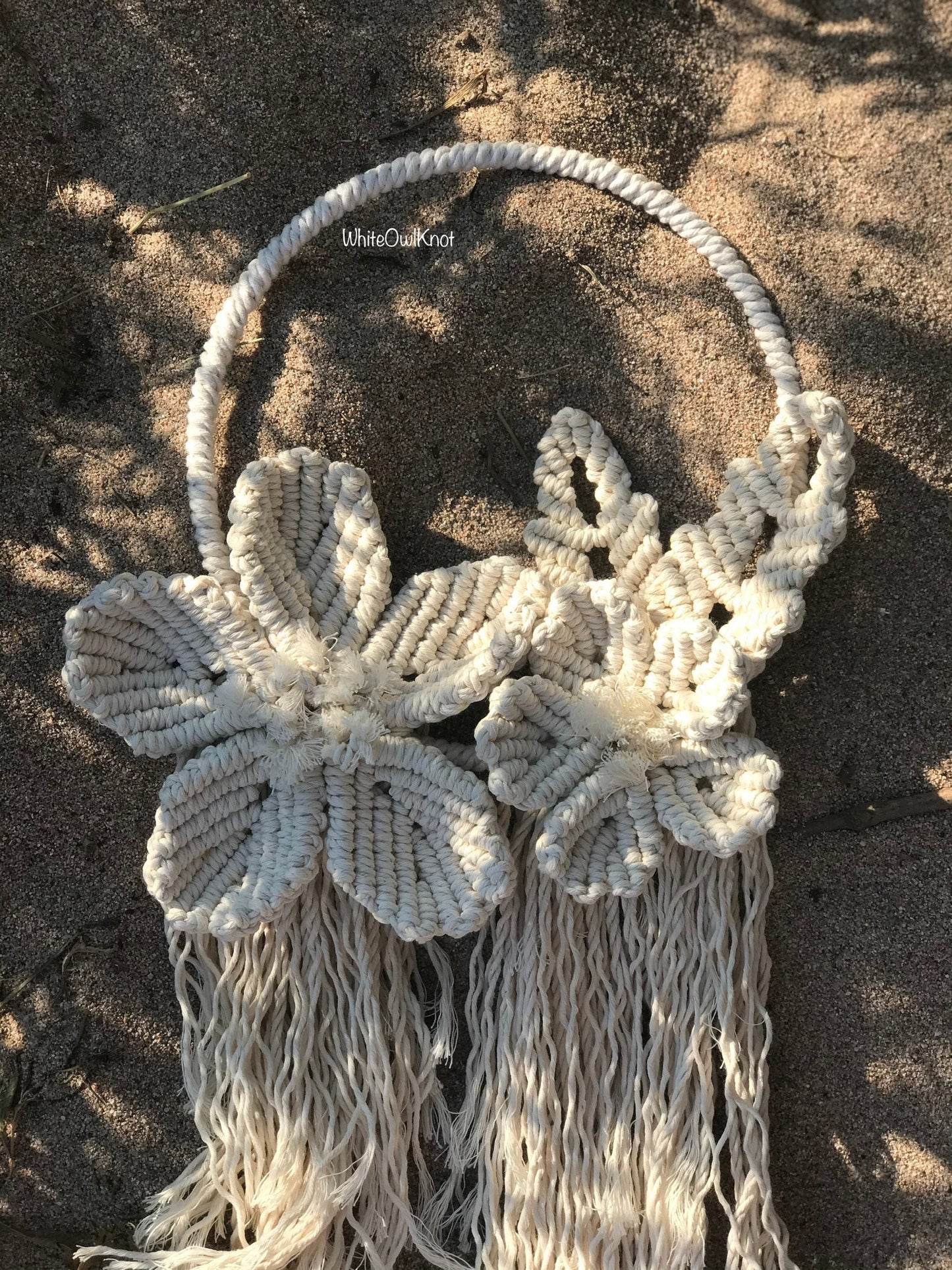 Macrame wall hanging with floral designs on a sandy background