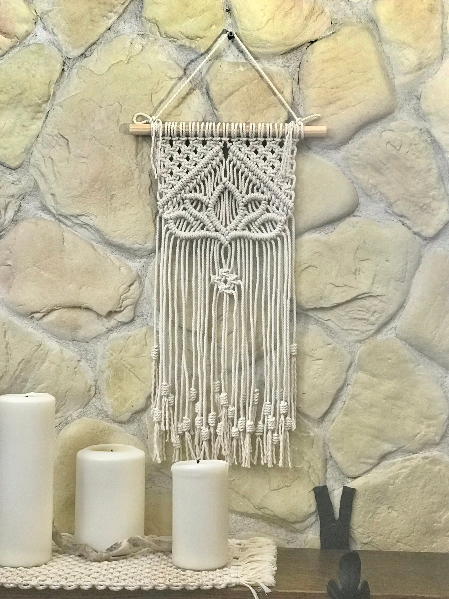 Macrame wall hanging on a stone wall with candles below