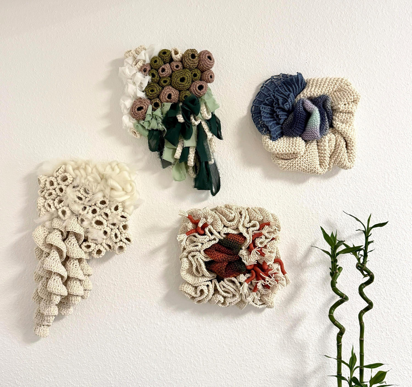 Four crocheted and macrame wall art pieces on a white background with a plant in the corner.