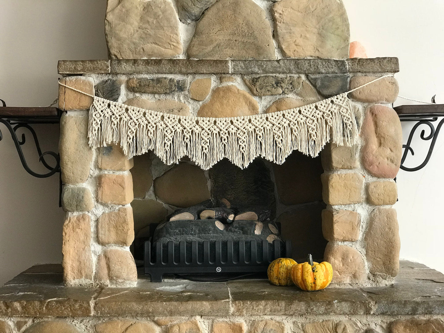 Stone fireplace with a decorative macrame banner and pumpkins on a mantel.