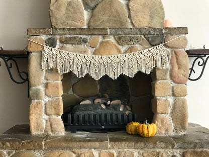 Stone fireplace with a decorative macrame banner and pumpkins on a mantel.