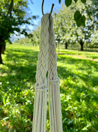 Braided rope hanging outdoors with trees and grass in the background